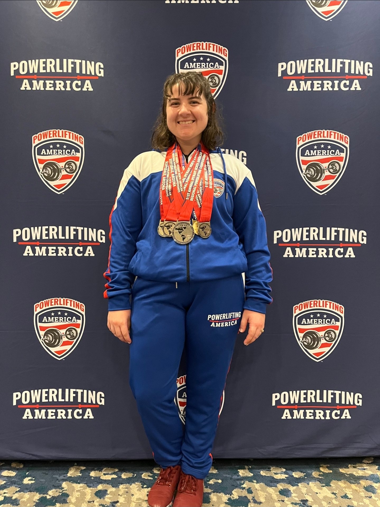 Emily with a stack of medals at a Powerlifting America championship
