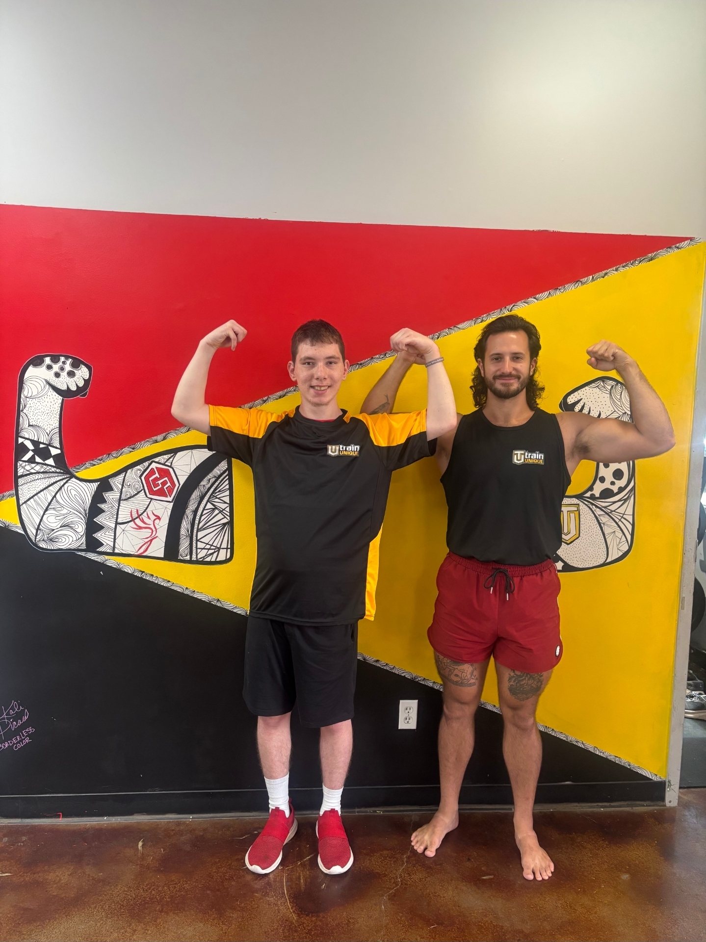 Garret and one of his athletes flexing in front of the mural at the Lafayette gym