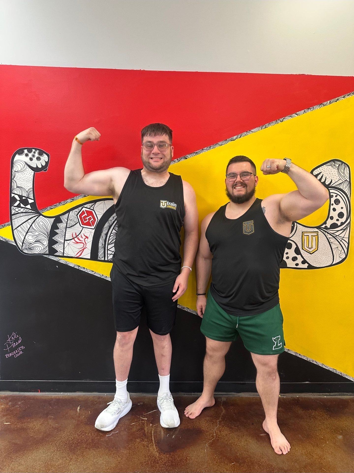 Jessie and one of his athletes flexing in front of the mural at the Lafayette gym