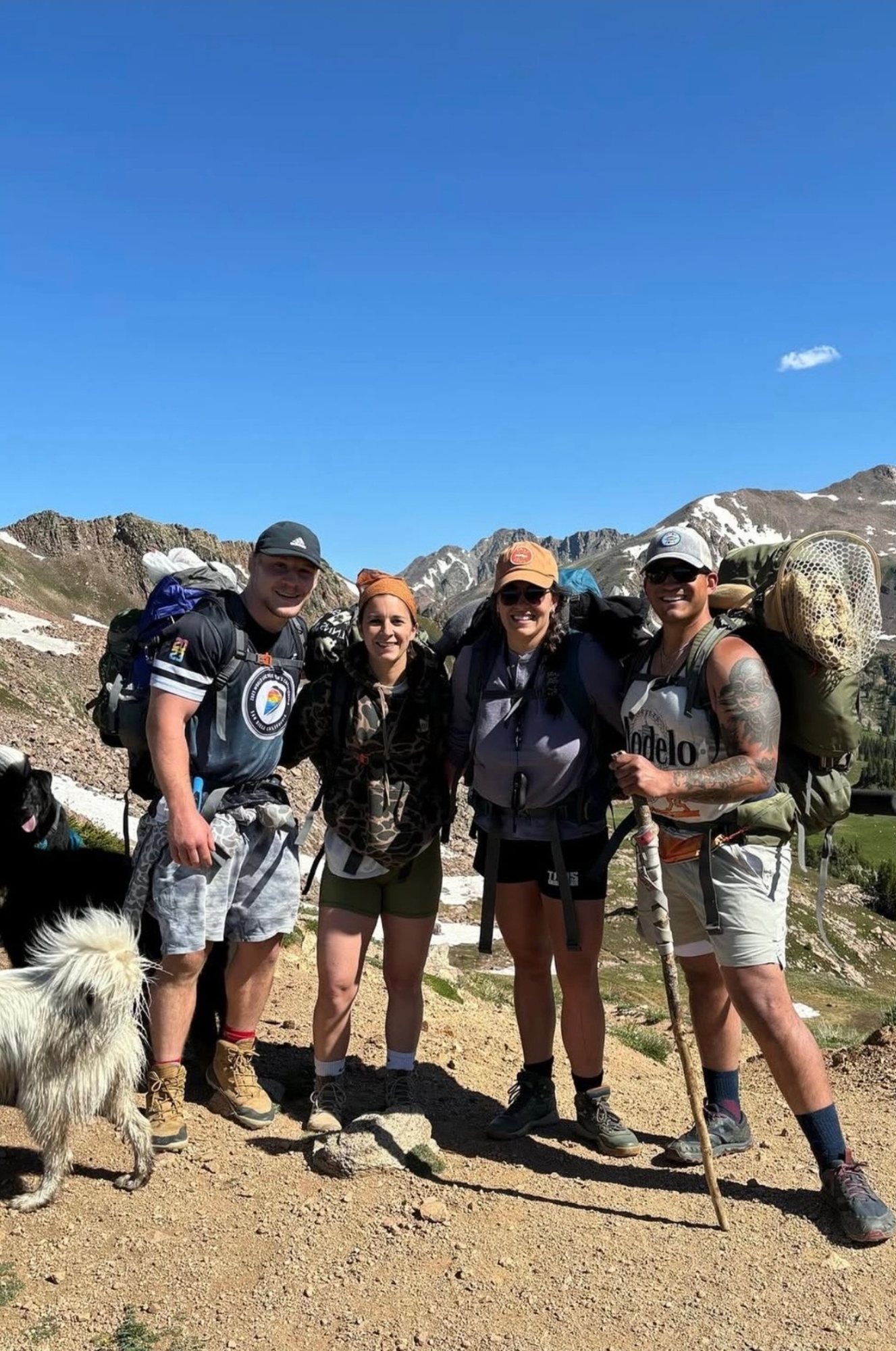 Madison with three friends and two dogs on a high mountain trail, packs on