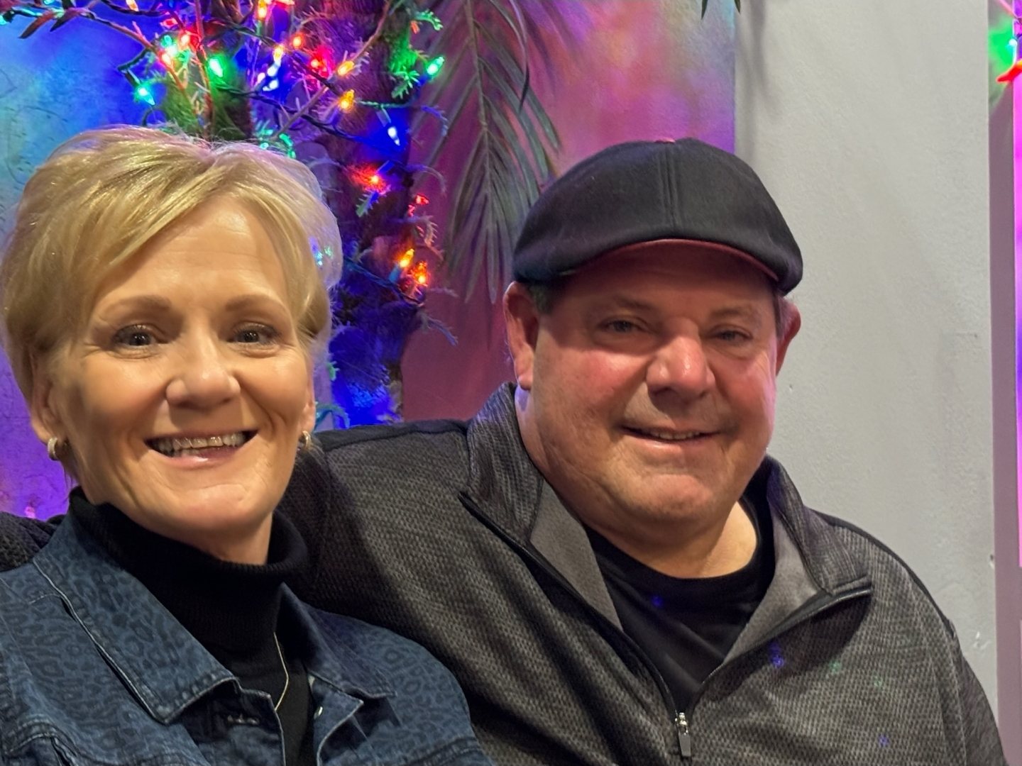 Paul in a flat cap, smiling, colored lights behind him