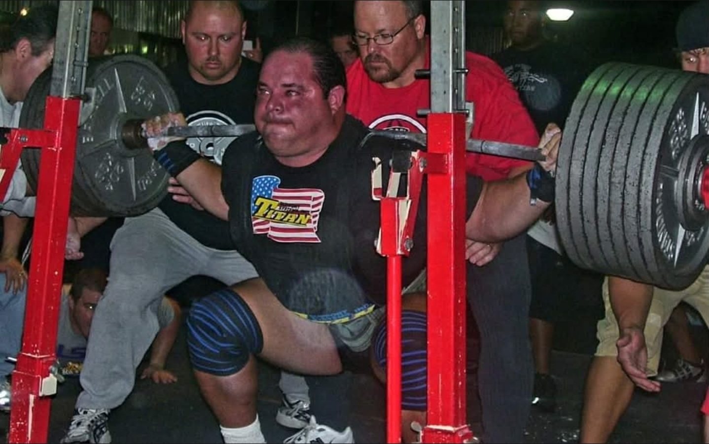 Paul deep in a heavy squat at a meet, spotters on both sides