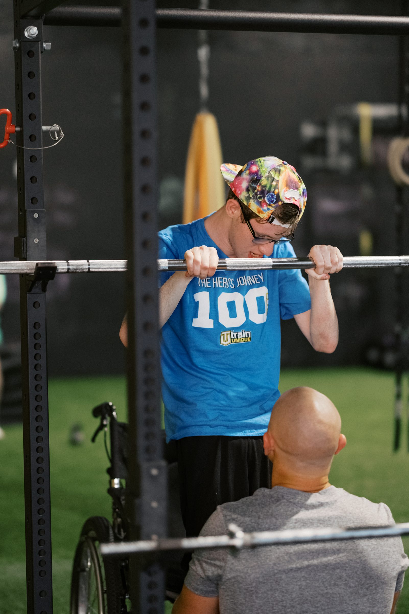 An athlete gripping the bar in the rack, his coach spotting from his wheelchair