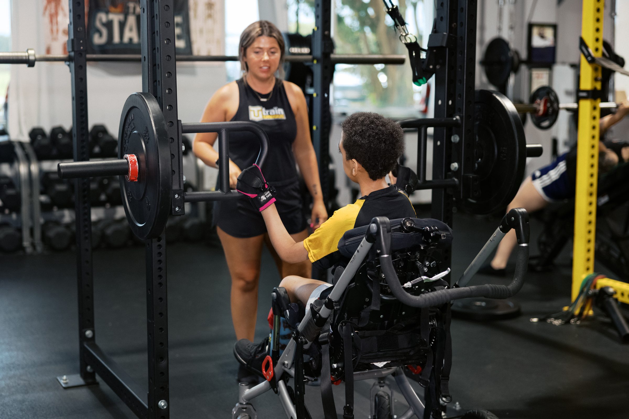 A coach at the loaded barbell rack with an athlete in his standing chair